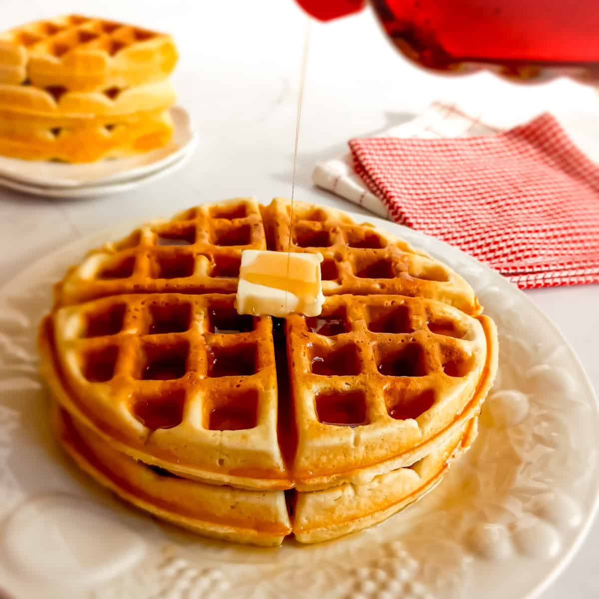 a double stack of Amish waffles on a plate with a pat of butter on top and drizzling syrup over them.