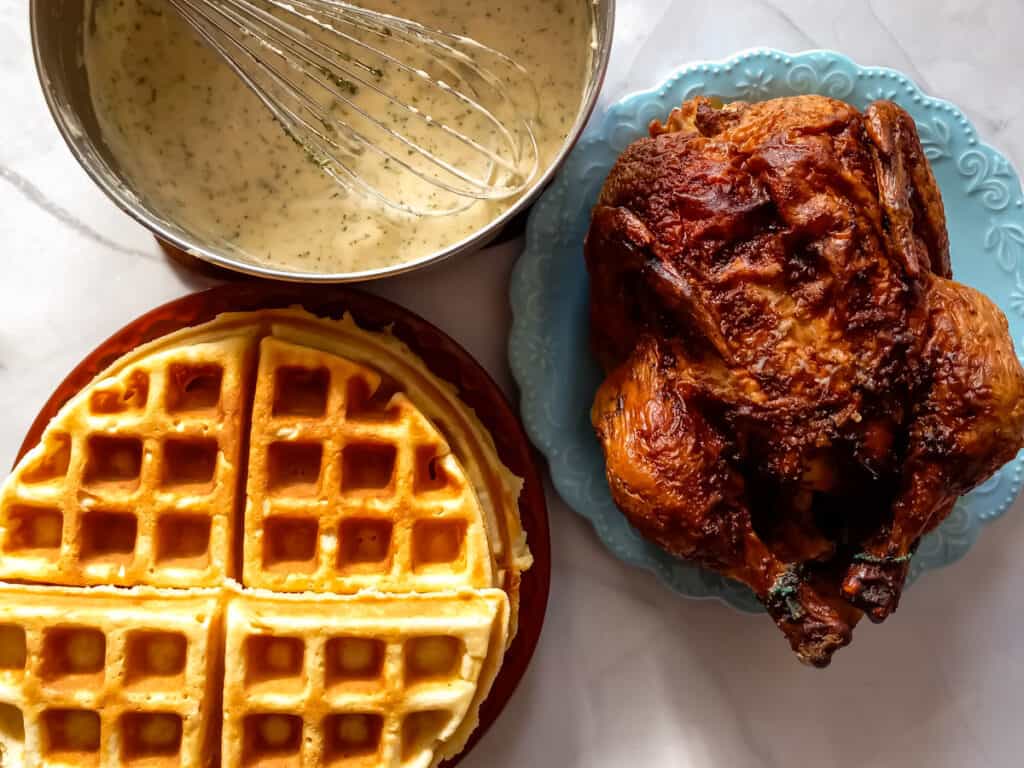 a stack of waffles, a pot with gravy, and a whole rotisserie chicken.