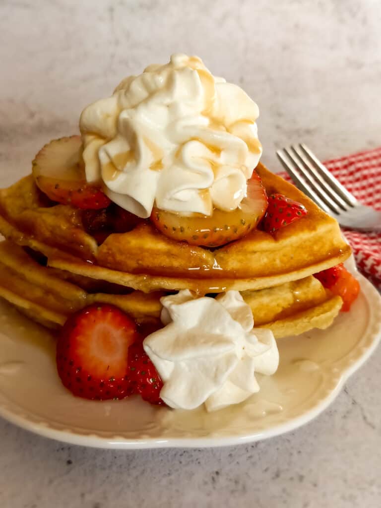 waffles topped with strawberries, whipped cream, and syrup.