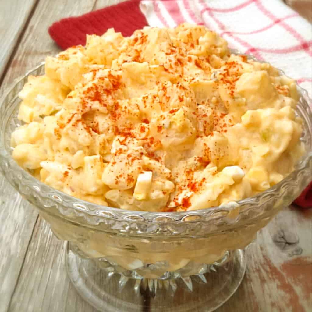 a glass bowl of Amish potato salad sprinkled with paprika.