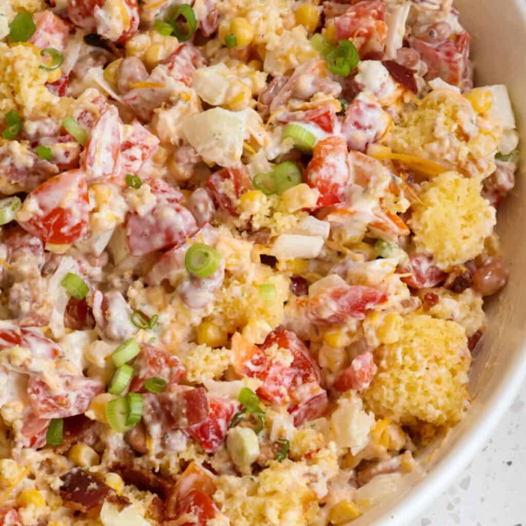 a bowl of cornbread salad with bacon, tomatoes, green onions, and dressing on top.