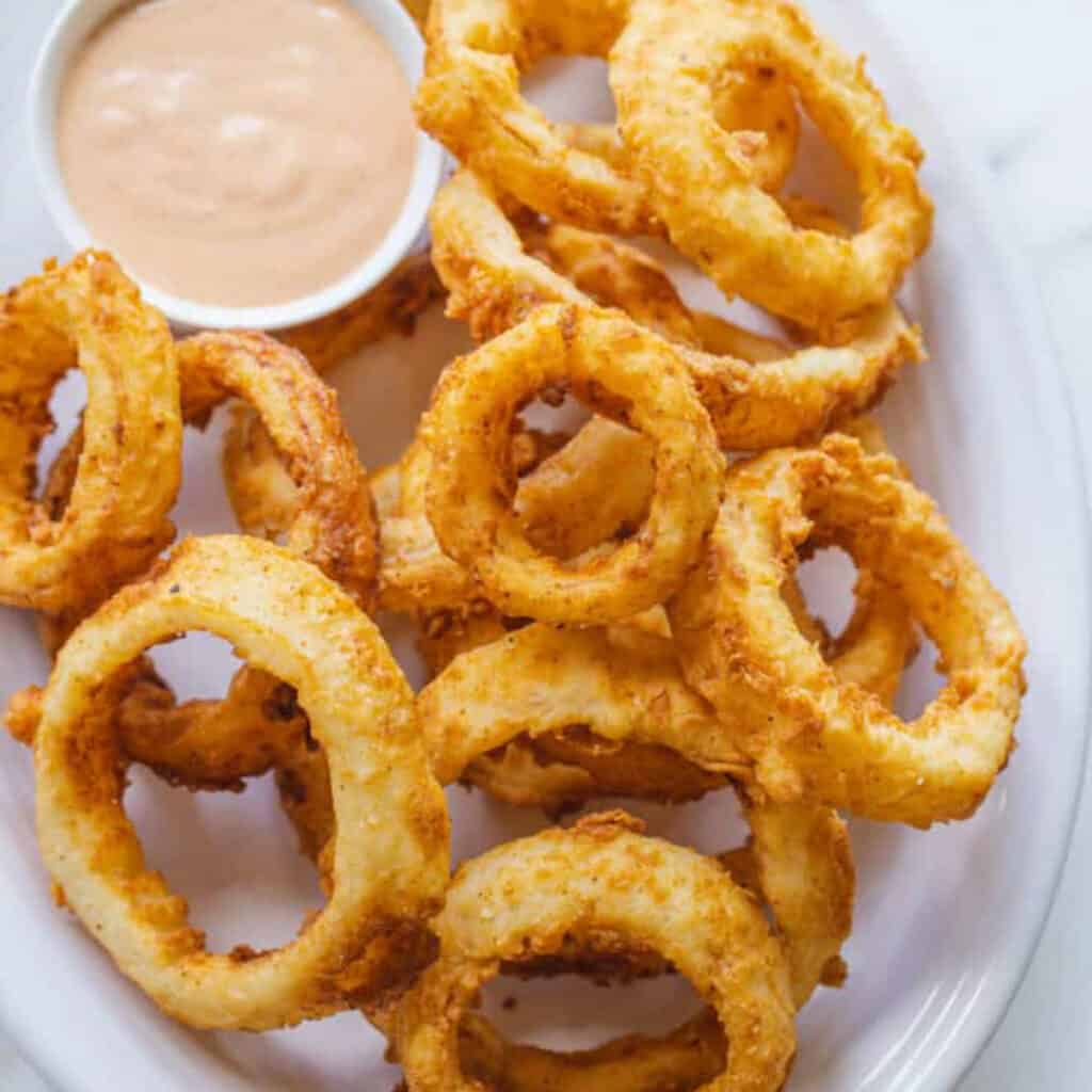 a plate of crispy onion rings with dip.