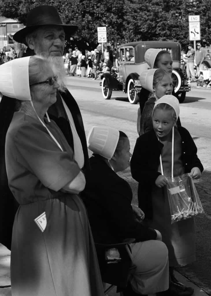 Amish man, woman, and girls watching a parade.