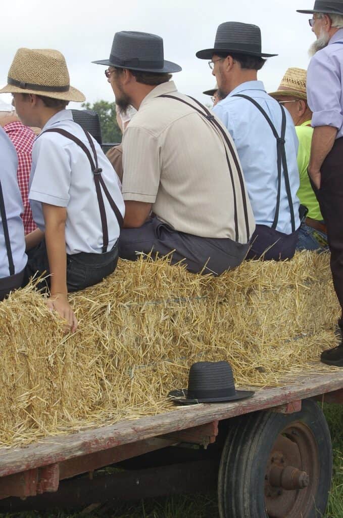 Amish men sitting on straw bales on a wagon.