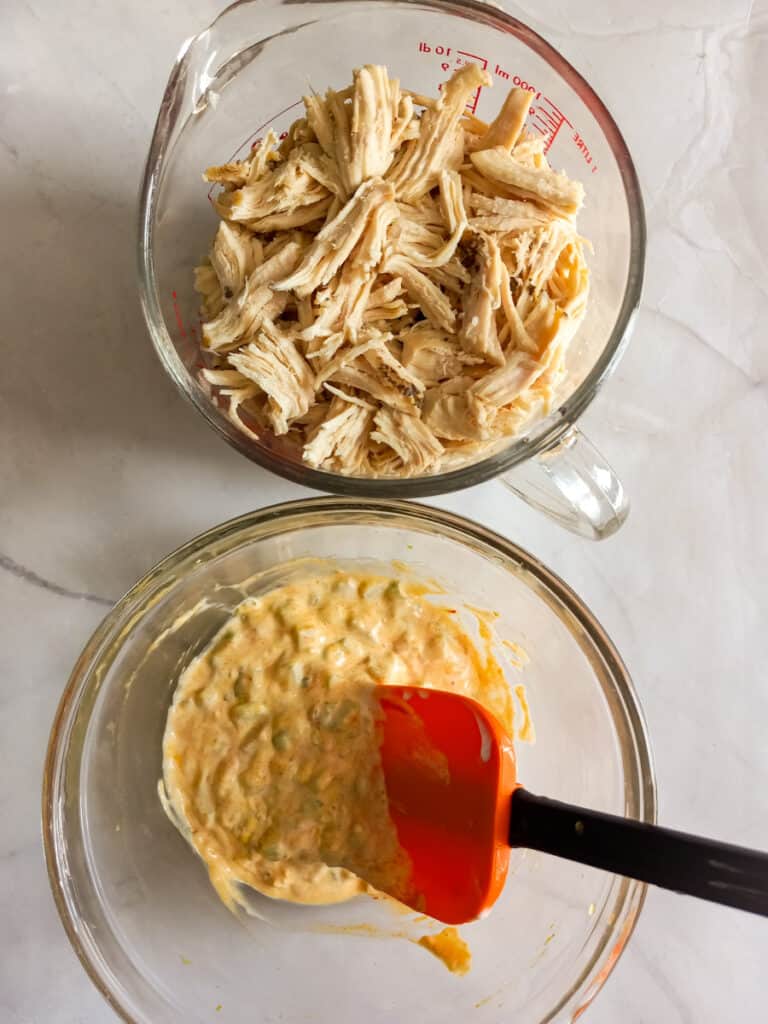 a bowl of shredded chicken and another bowl of dressing ingredients.