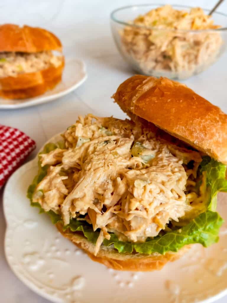 a croissant chicken salad sandwich and a bowl of chicken salad in the background.