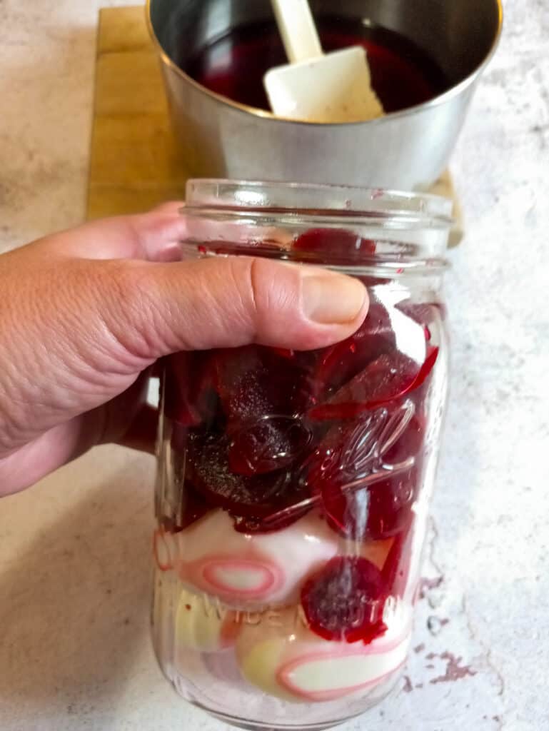 eggs in a jar with beets on top, brine in a pot.