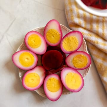 red beet eggs in a round circle on a plate with beet slices in the middle.