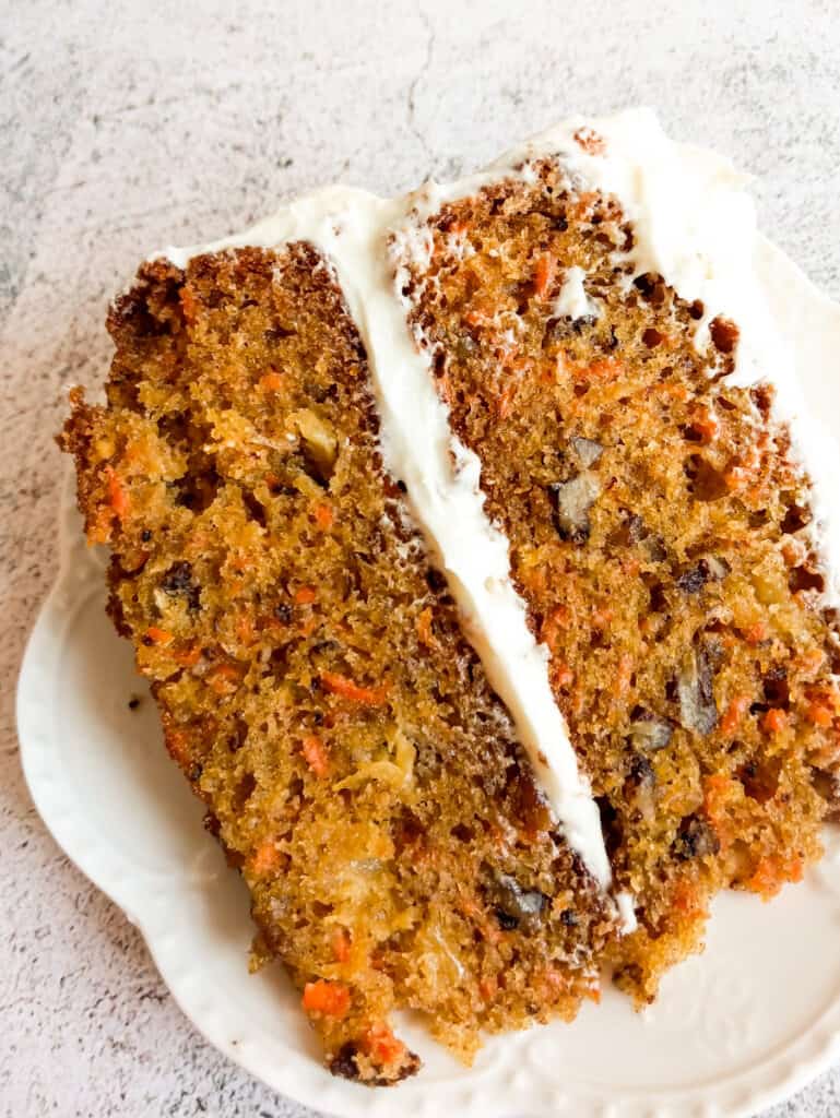 close up photo of a slice of layered carrot cake with cream cheese frosting.