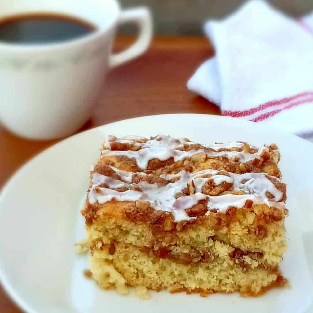 a slice of cinnamon streusel coffee cake on a small plate with a cup of coffee on the side.