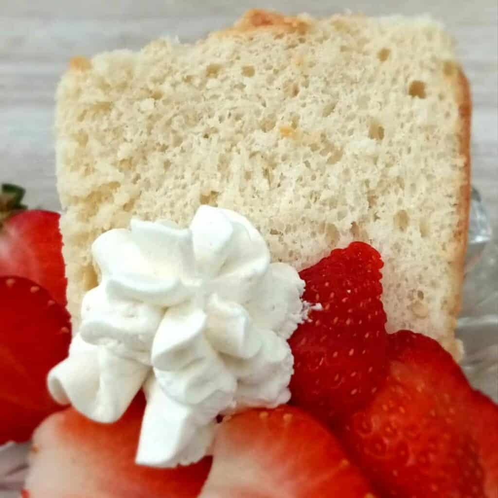 a slice of angel food cake on a plate with sliced strawberries and whipped cream.