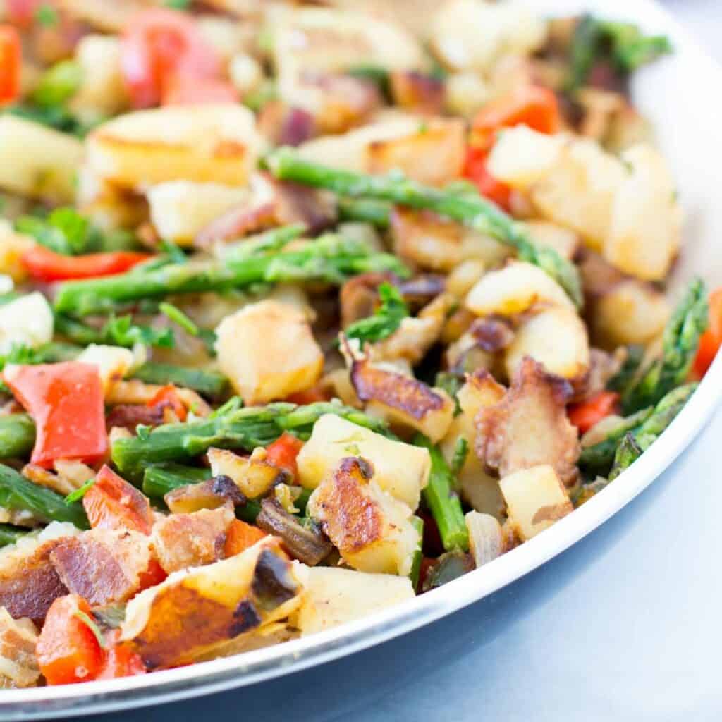 a skillet full of Caliente bacon potato hash with asparagus.