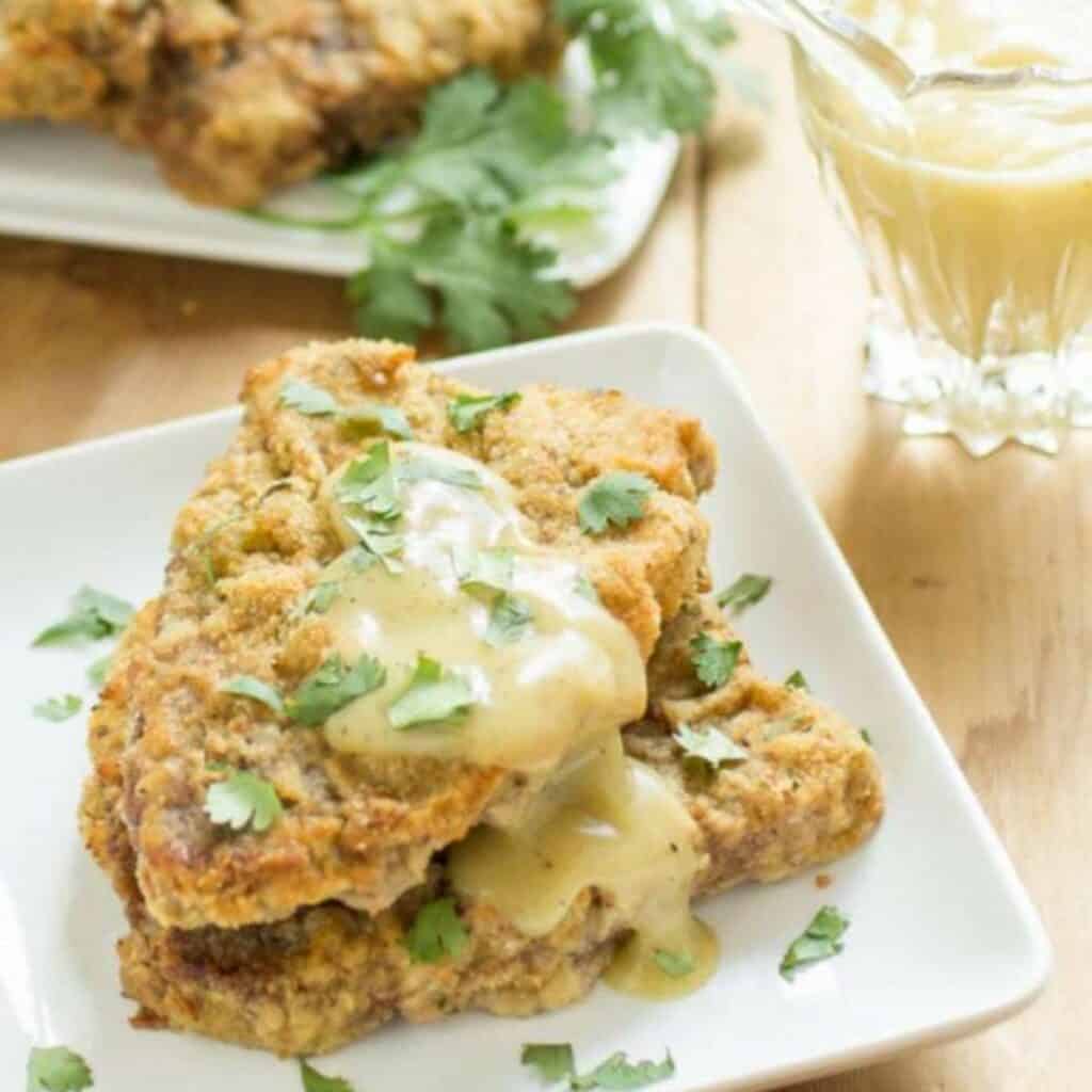 two chicken fried steaks on a plate with a bit of gravy and herbs.