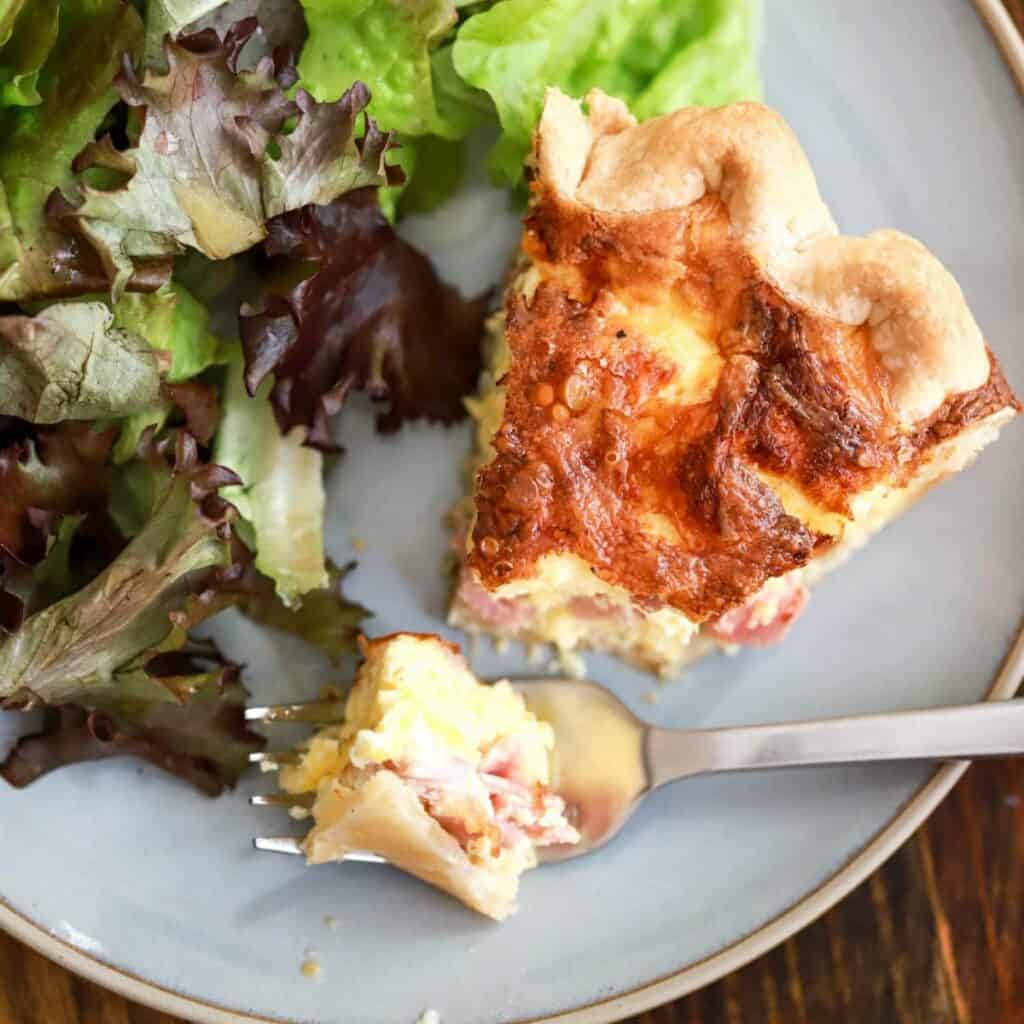 slice of quiche and salad greens on a plate.