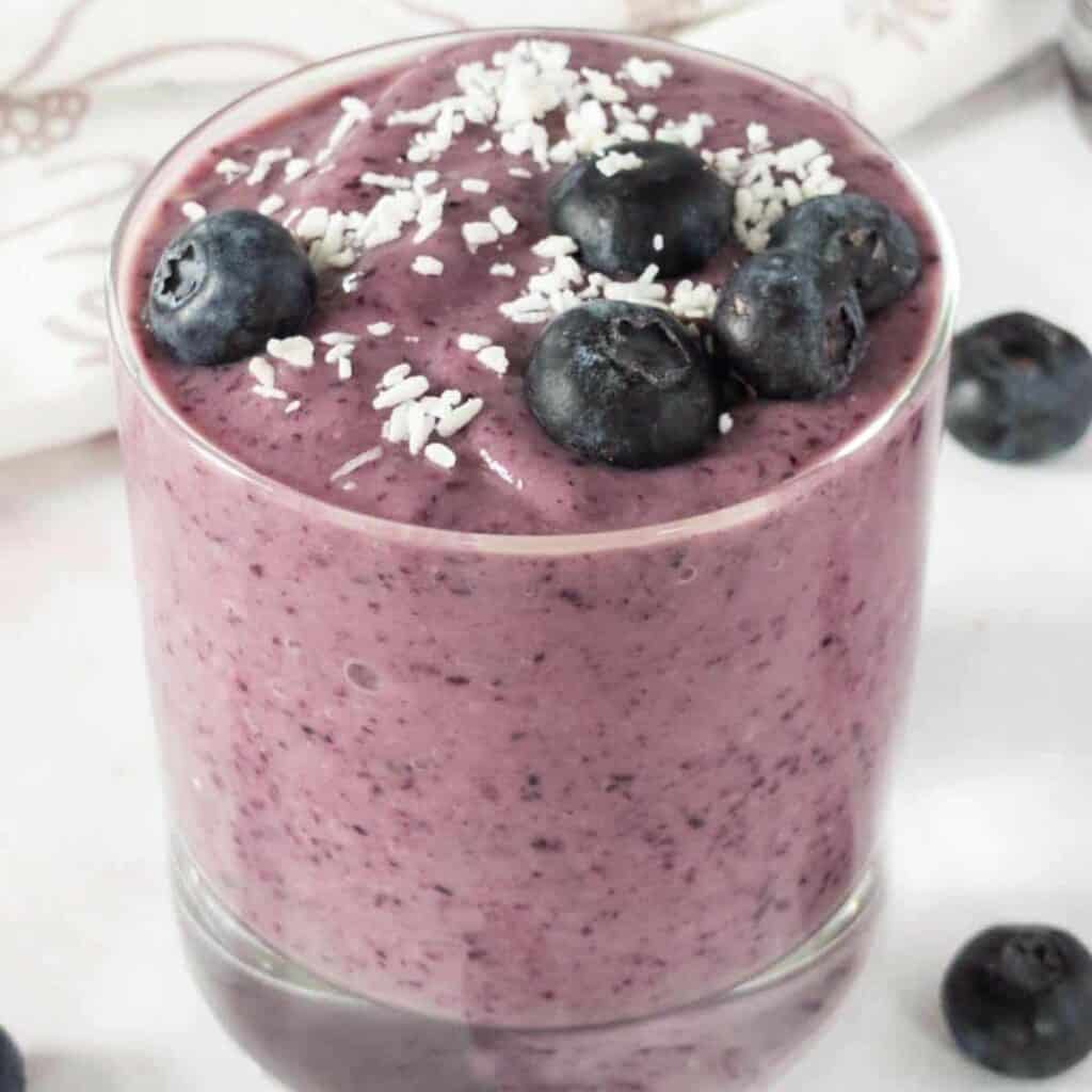 a glass cup full of blueberry avocado smoothie and blueberries on top.