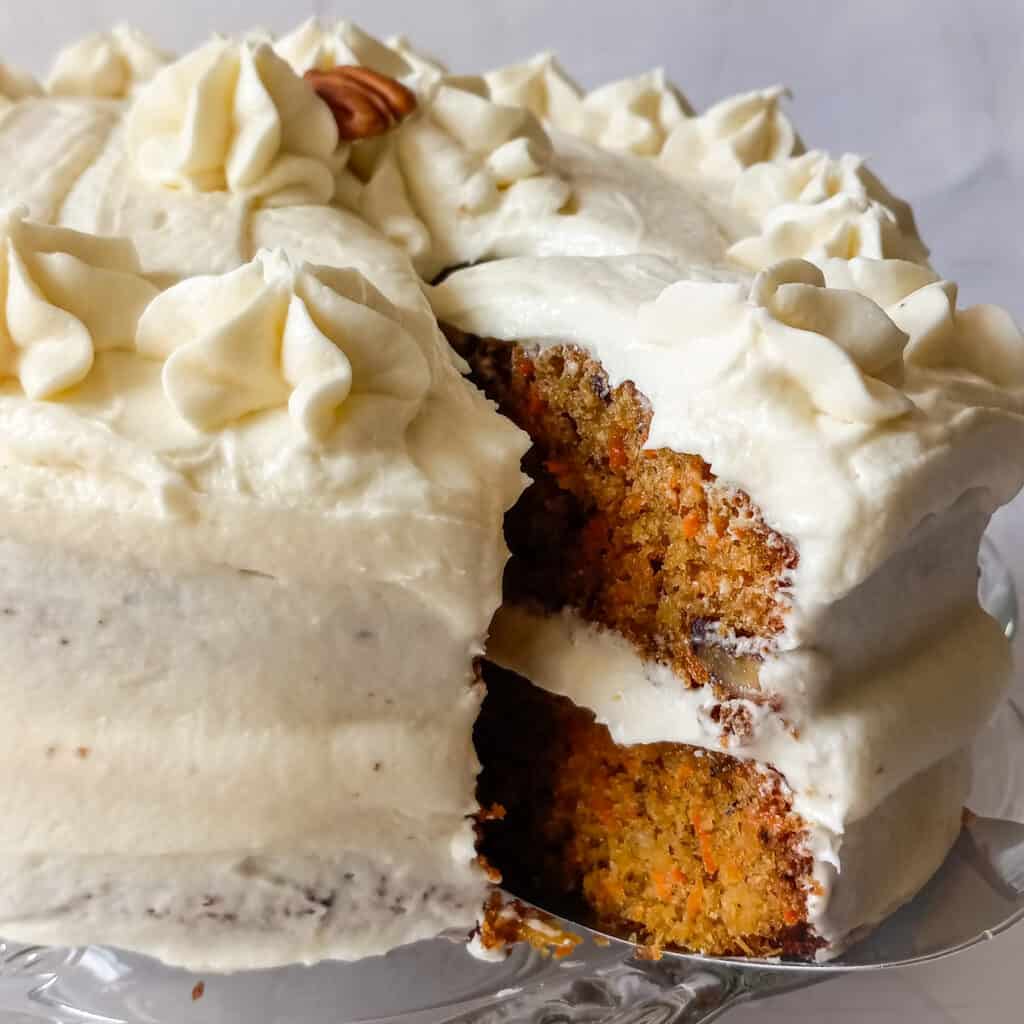 round layered carrot cake on a platter, a slice is cut and pulled back so you can see the inside.