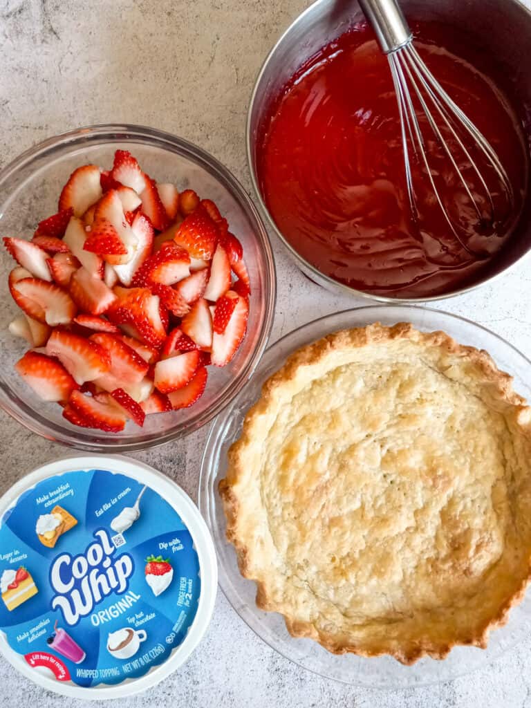 a pan with the jello sauce, bowl of sliced strawberries, empty pie crust, and a tub of Cool Whip.