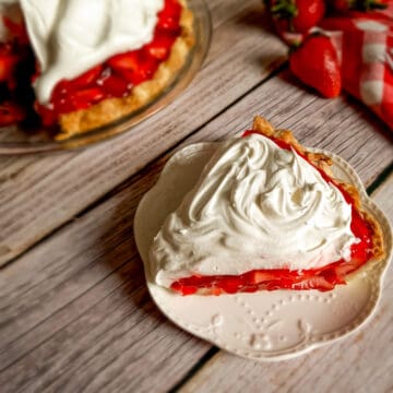 a slice of fresh strawberry pie on a small plate, remaining pie in the background.