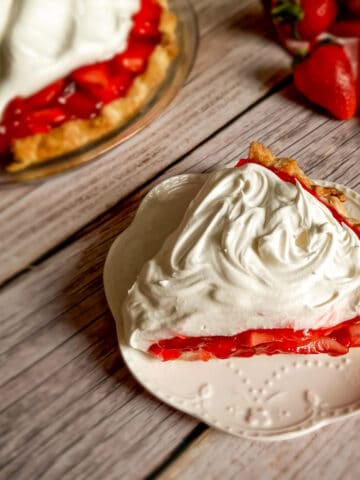 a slice of fresh strawberry pie on a small plate, remaining pie in the background.