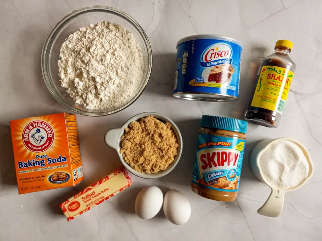 Ingredients: flour, baking soda, brown sugar, white sugar, Crisco, butter, peanut butter, eggs, and vanilla.