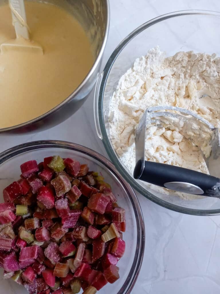 crumbling shortbread ingredients in a bowl, chopped rhubarb in another bowl, and custard filling in a third bowl.