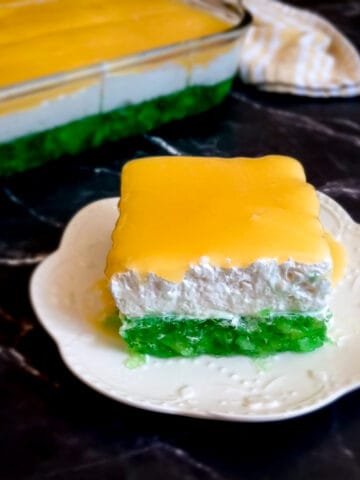 a plate of layered Indiana jello salad on a small plate with the remaining dish in the background on a black backdrop.