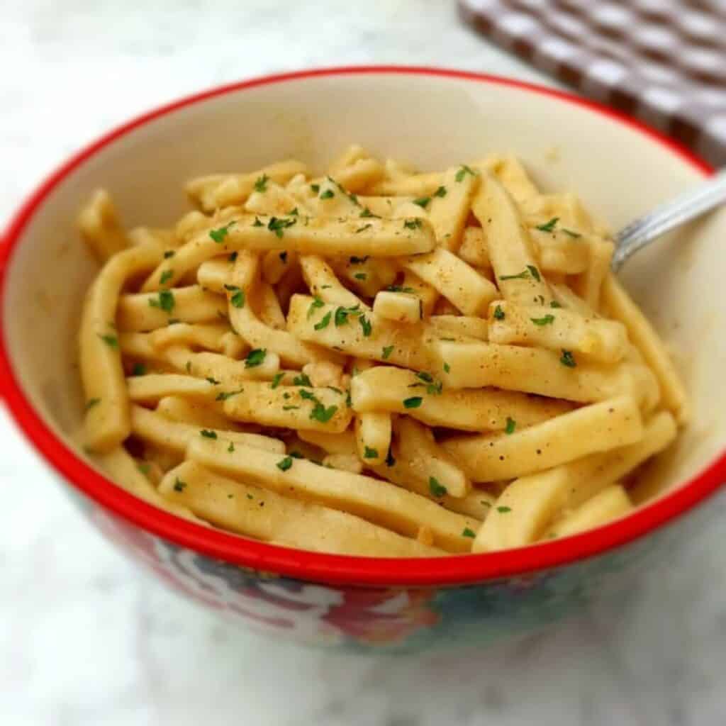 a bowl of buttered noodles with parsley on top.