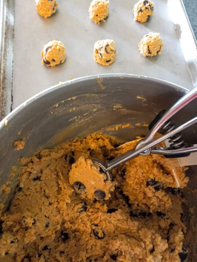 cookie dough in a bowl and scooping some onto a cookie tray.