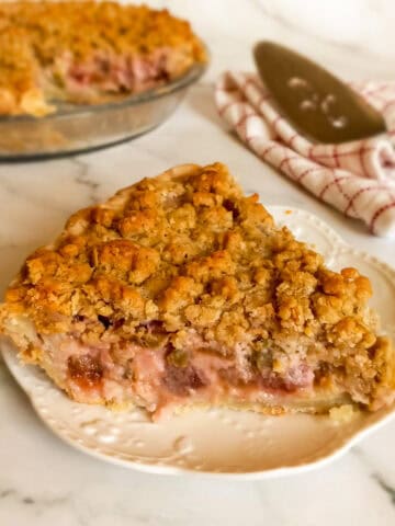 rhubarb pie with crumb topping on a plate and the remaining pie in the background.
