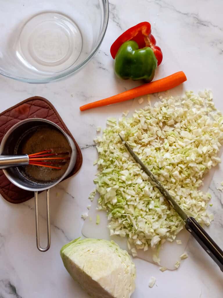 chopping cabbage, dressing in a saucepan, and a bowl to mix the ingredients.
