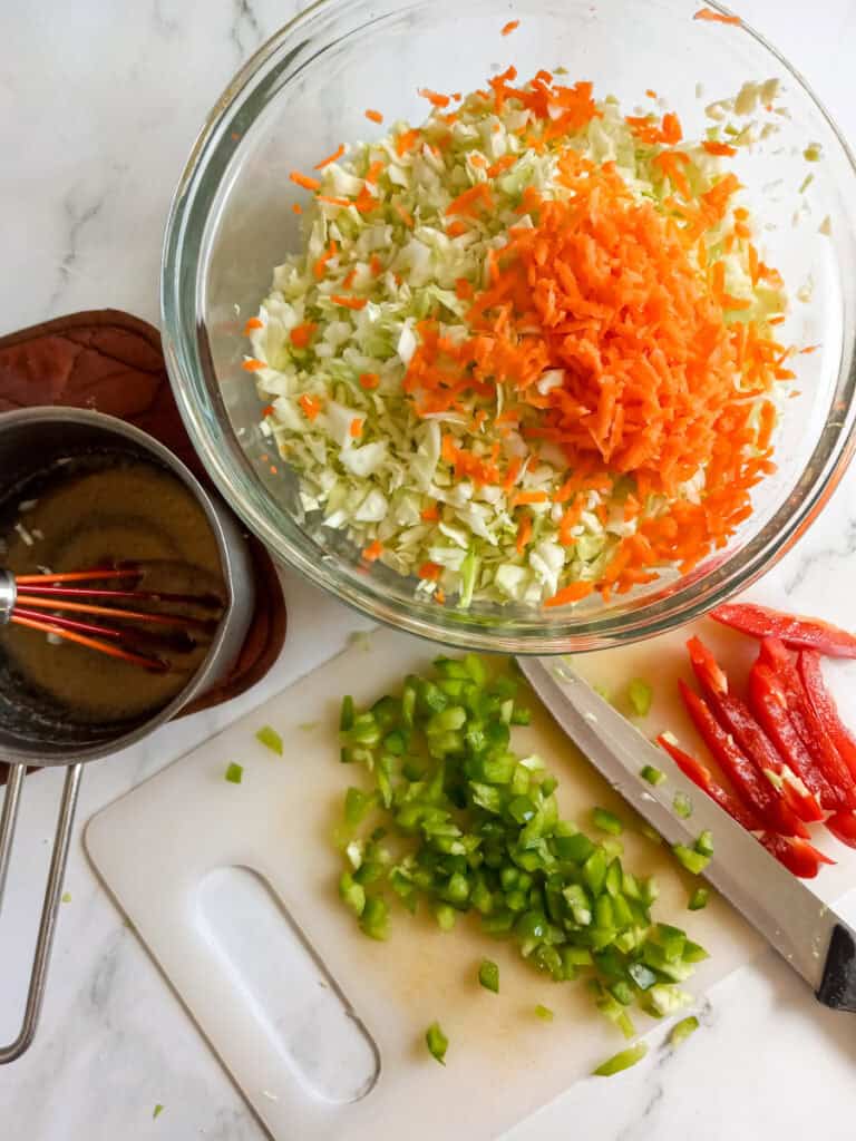 chopped vegetables in a bowl, chopping peppers on a cutting board, dressing on the side.