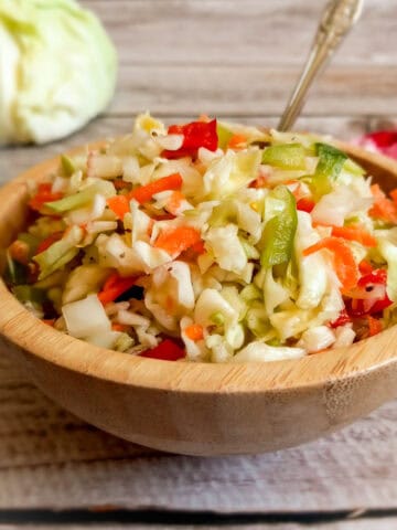 a small bowl full of pepper cabbage ready to eat, cabbage head and green pepper in the background.