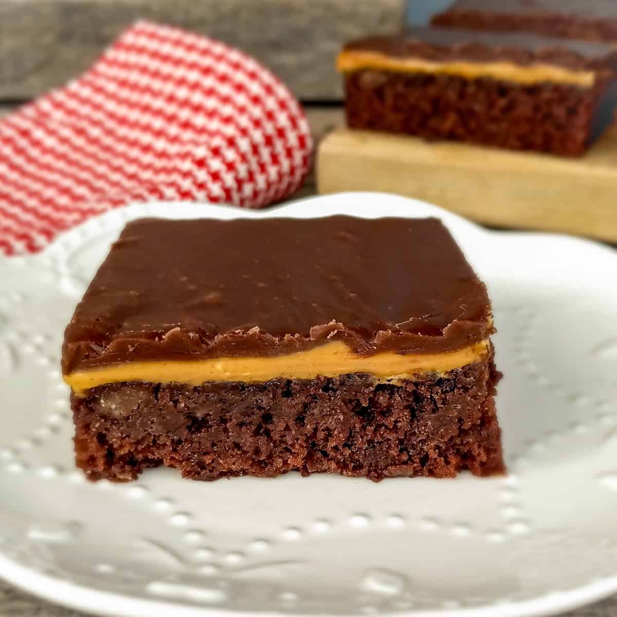 a three-layered chocolate peanut butter bar on a dish and some in the background.