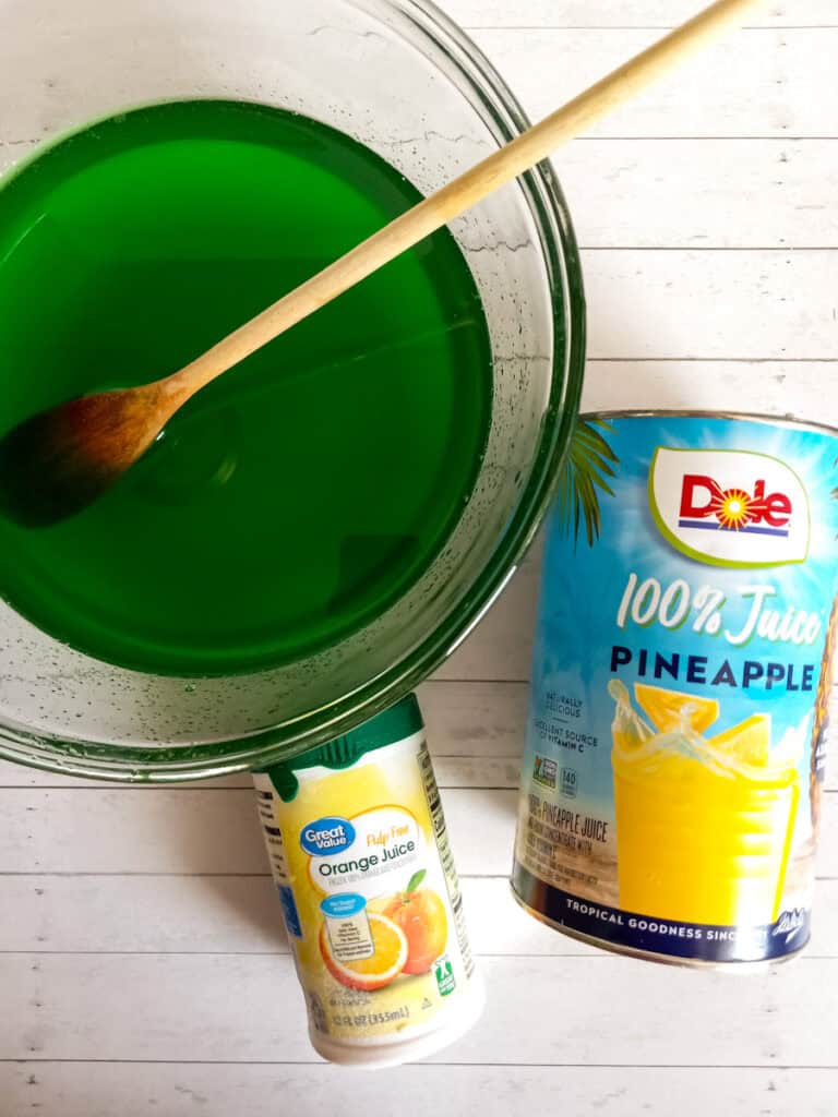 lime jello dissolved in water in a large bowl, a can of pineapple juice and orange concentrate.