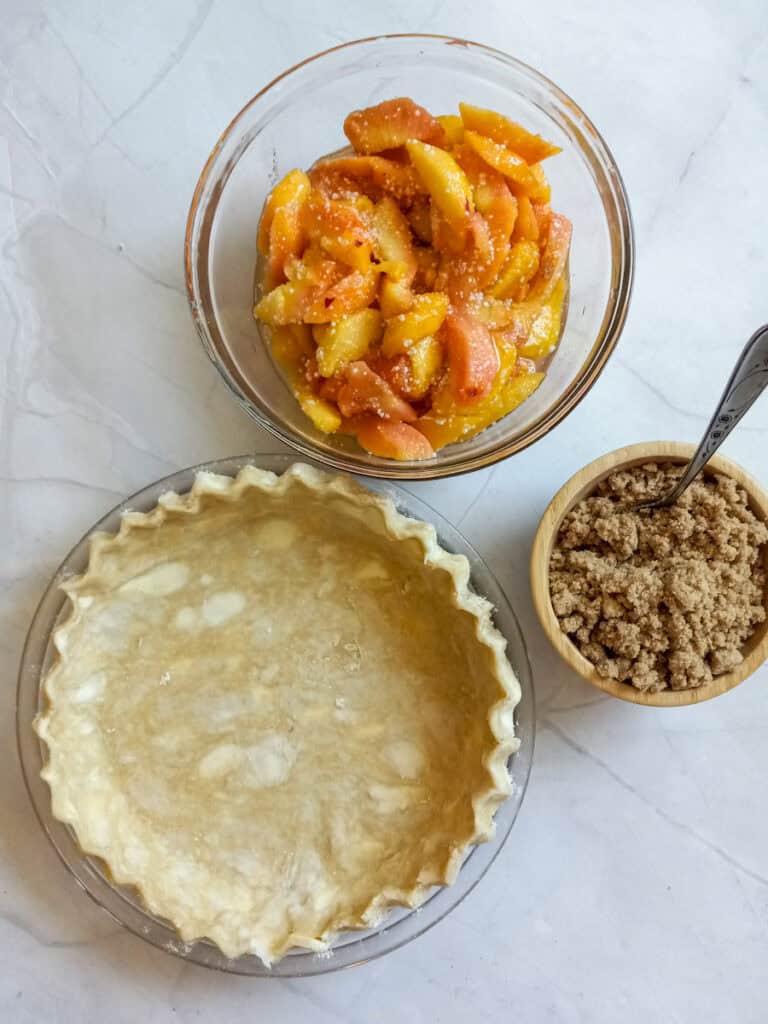 9" pie crust, crumble topping in a small bowl, and peach mixture in another bowl.