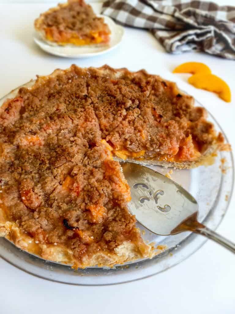 a slice taken out of the 9" peach pie with a pie server in its place.