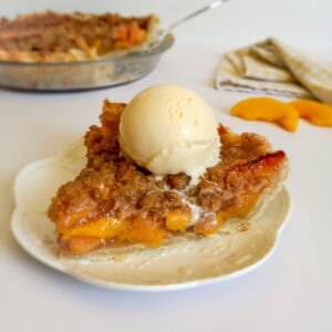 a slice of peach pie on a plate with a scoop of vanilla ice cream melting on the top.