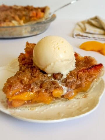 a slice of peach pie on a plate with a scoop of vanilla ice cream melting on the top.