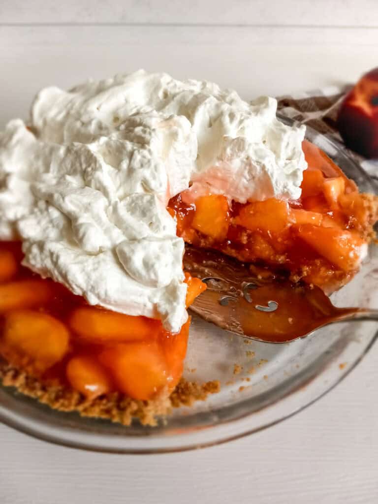 a whole Amish peach pie with graham cracker crust and whipped cream, with a slice removed.