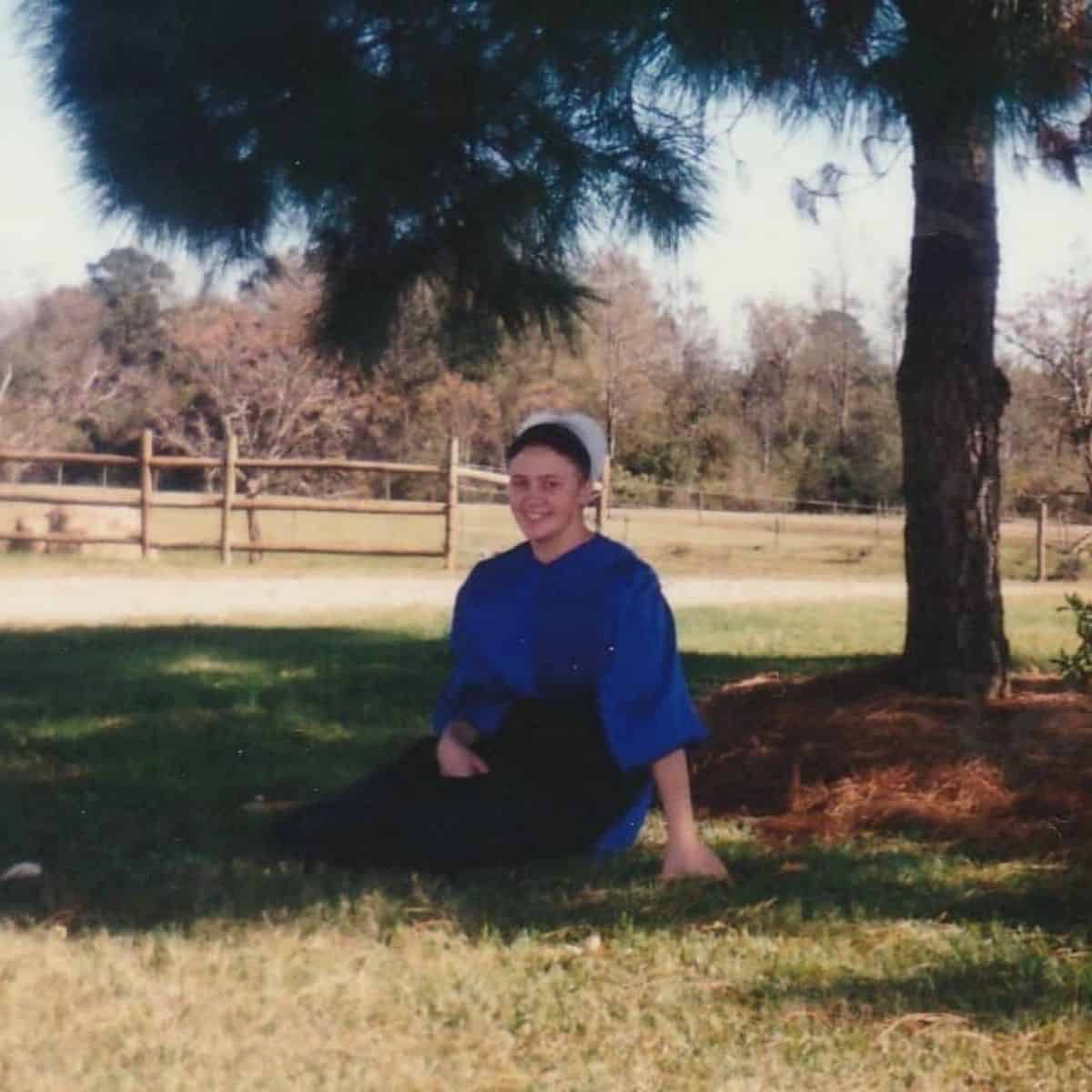 Amish girl sitting under a tree.