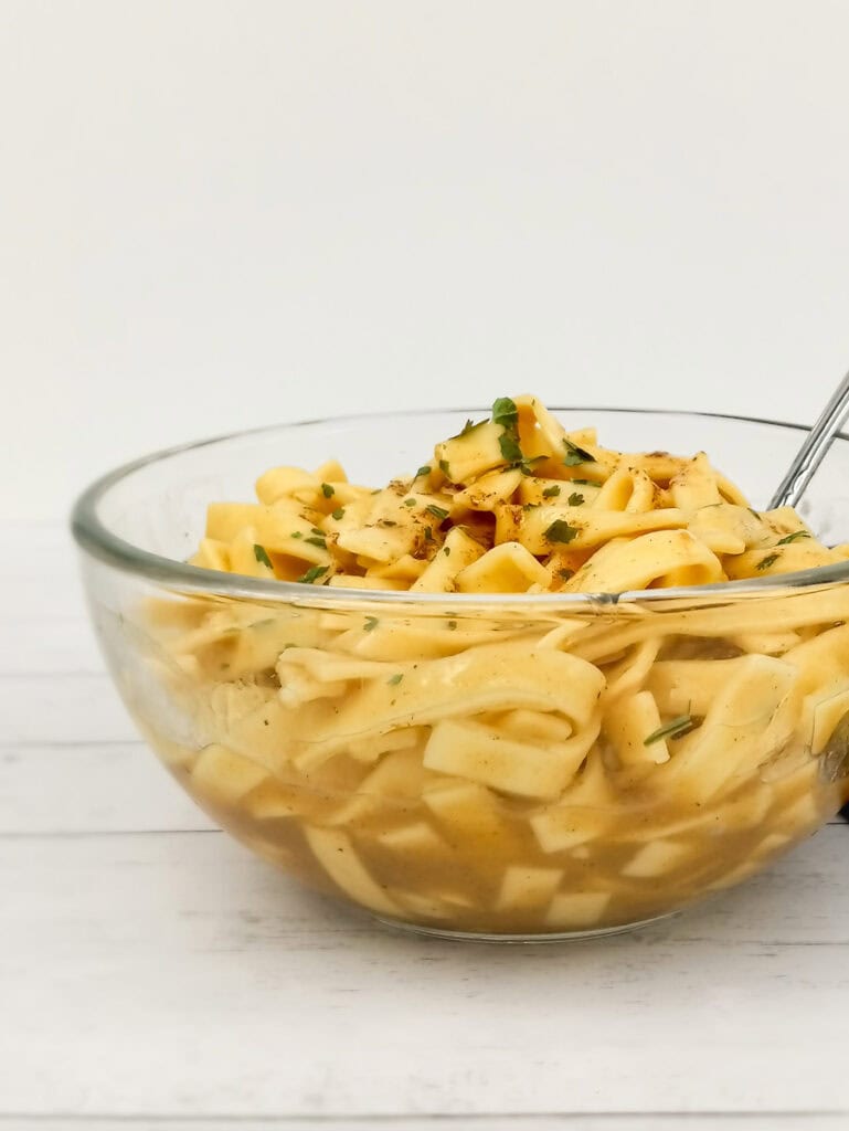 a side view of a clear bowl full of buttered egg noodles.