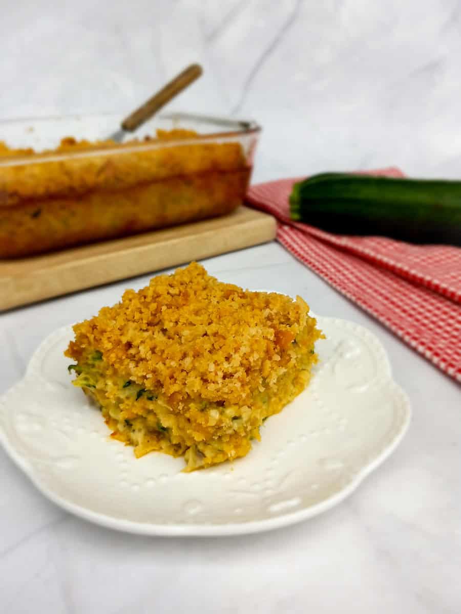 a slice of zucchini casserole on a plate and the remaining dish in the background.