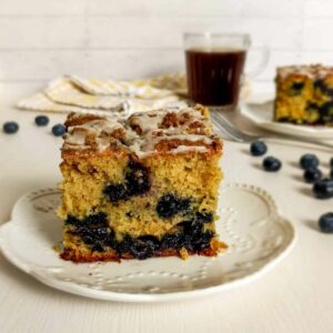 Two slices of Amish sour cream blueberry coffee cake on small plates, ready to enjoy with a cup of coffee.