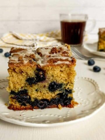 Two slices of Amish sour cream blueberry coffee cake on small plates, ready to enjoy with a cup of coffee.