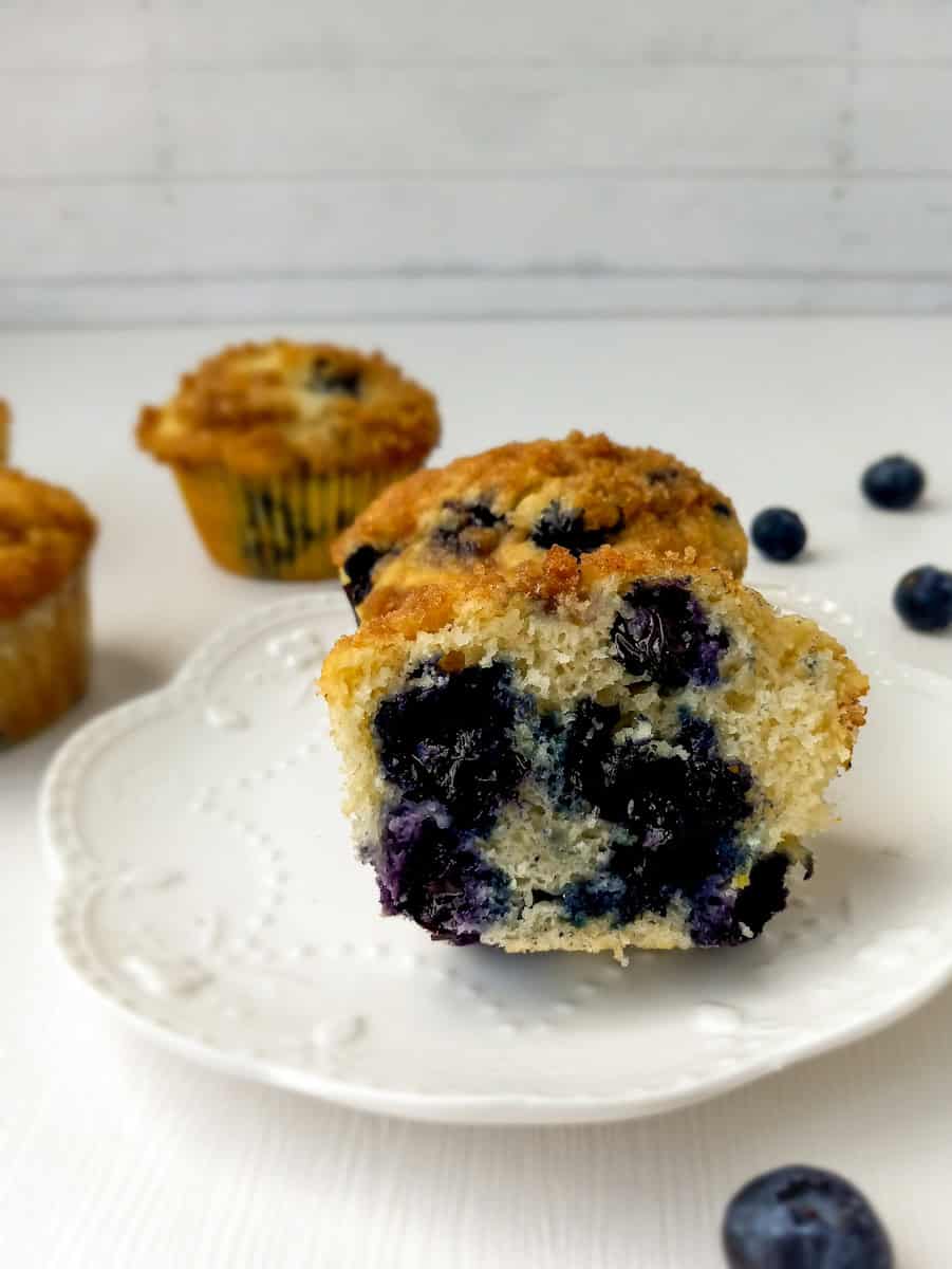 a blueberry muffin and one halved muffin on a plate.