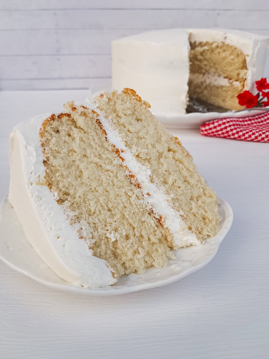 a large slice of fluffy white cake on a plate and the remaining layered cake in the background.