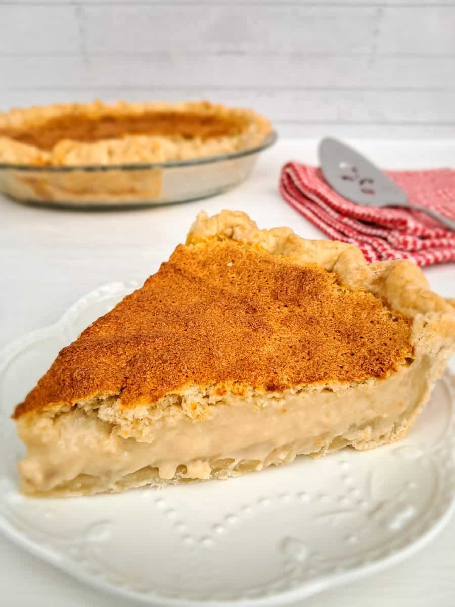 a slice of custard pie and the remaining pie in the background.