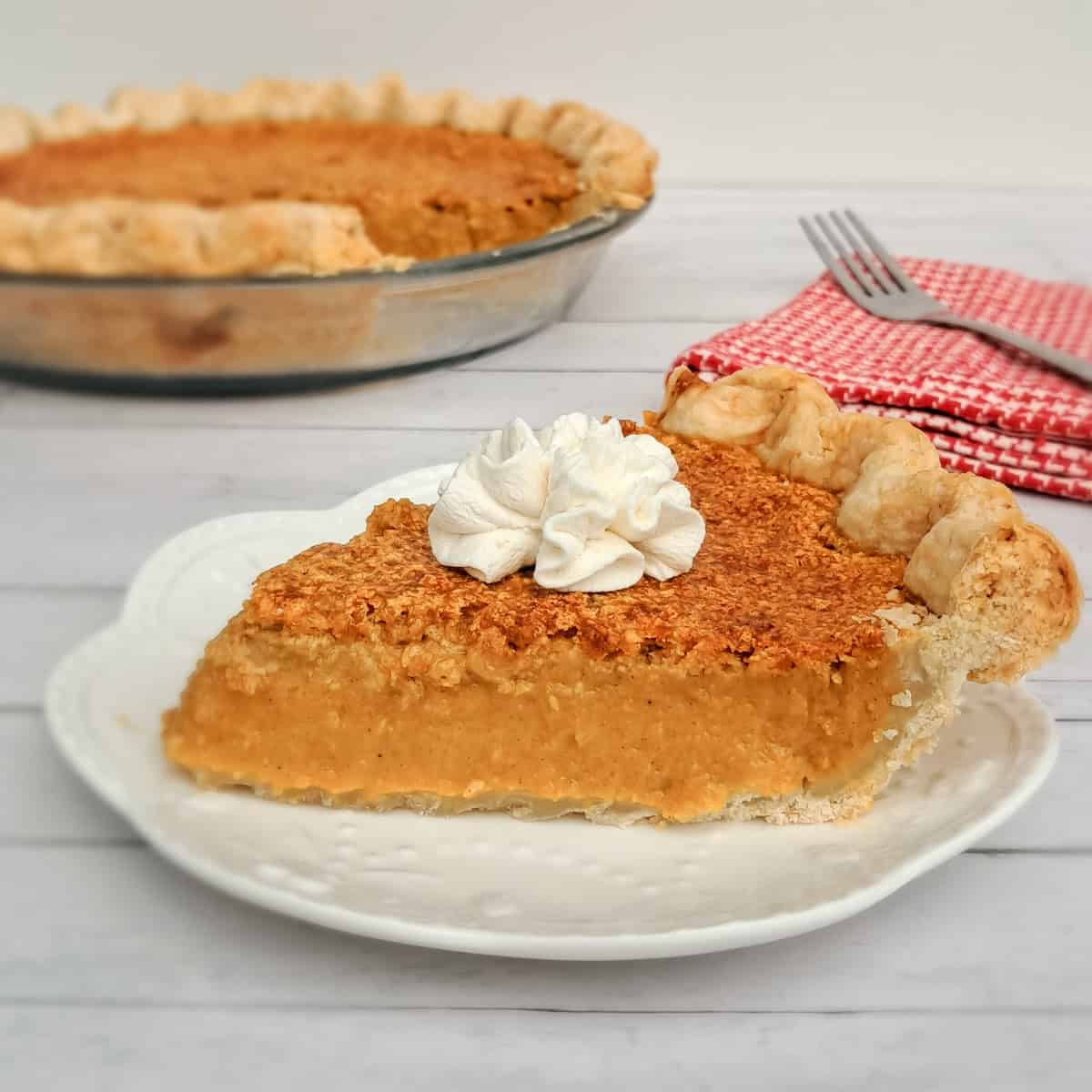 a slice of pumpkin pie with a dollop of whipped cream on a small plate.