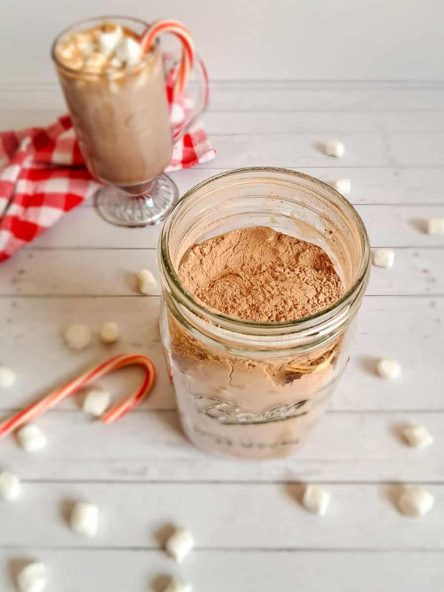 hot chocolate mix in a jar and a cup of hot chocolate in the background.