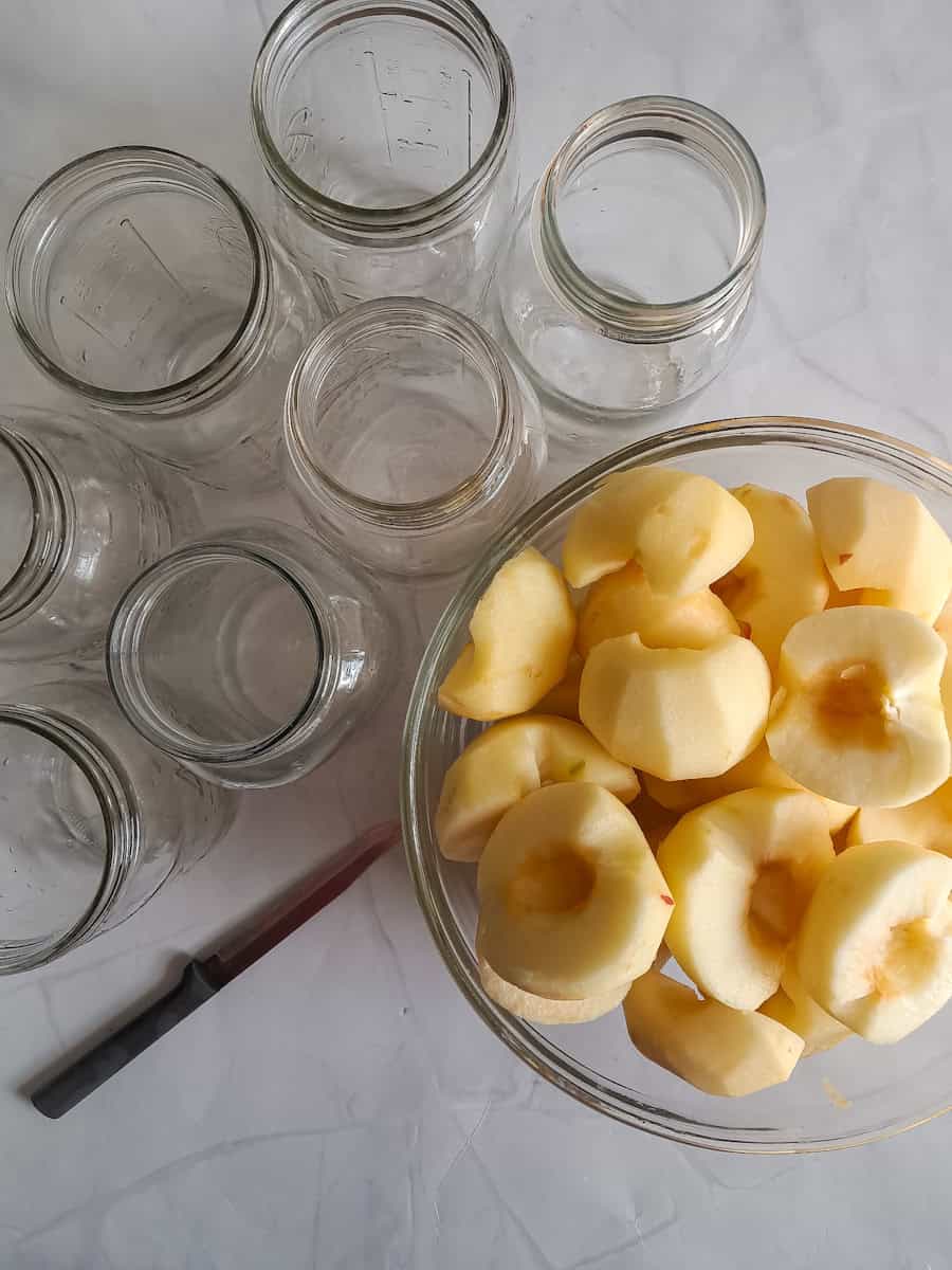 peeled apples in a large bowl and empty jars waiting to be filled.